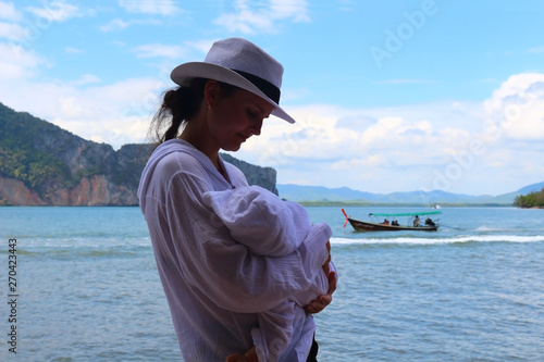 A young girl on the beach of the sea breastfeeds a child.