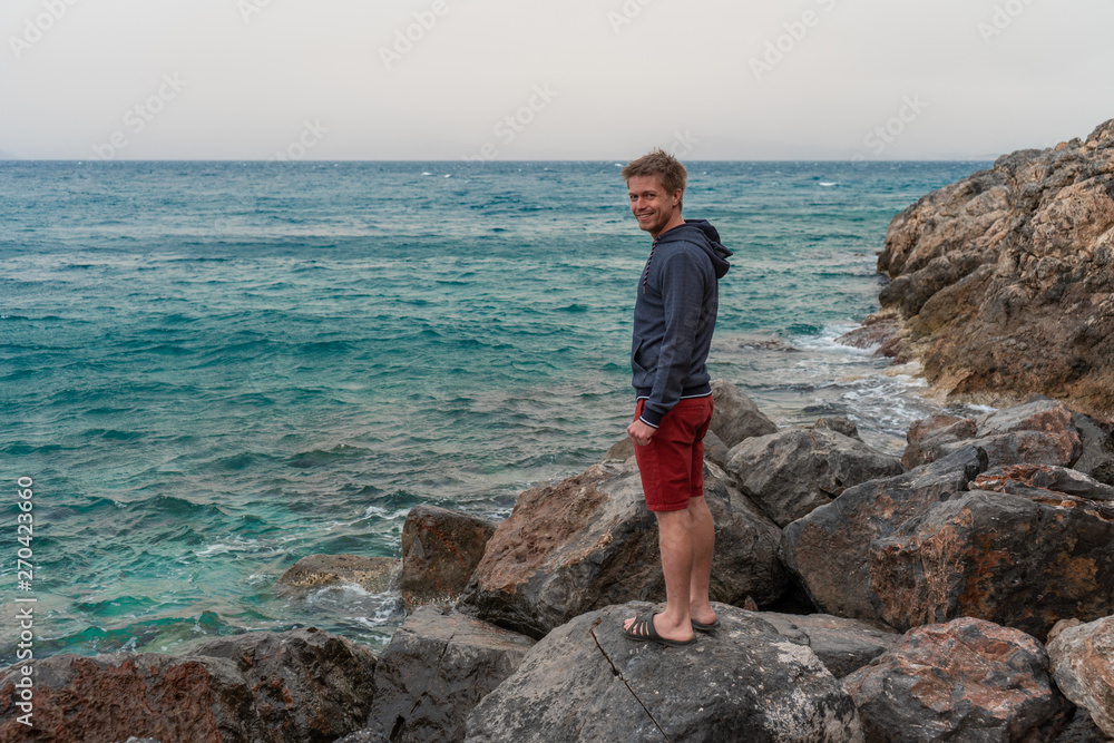 a young man stands on the rocks by the sea