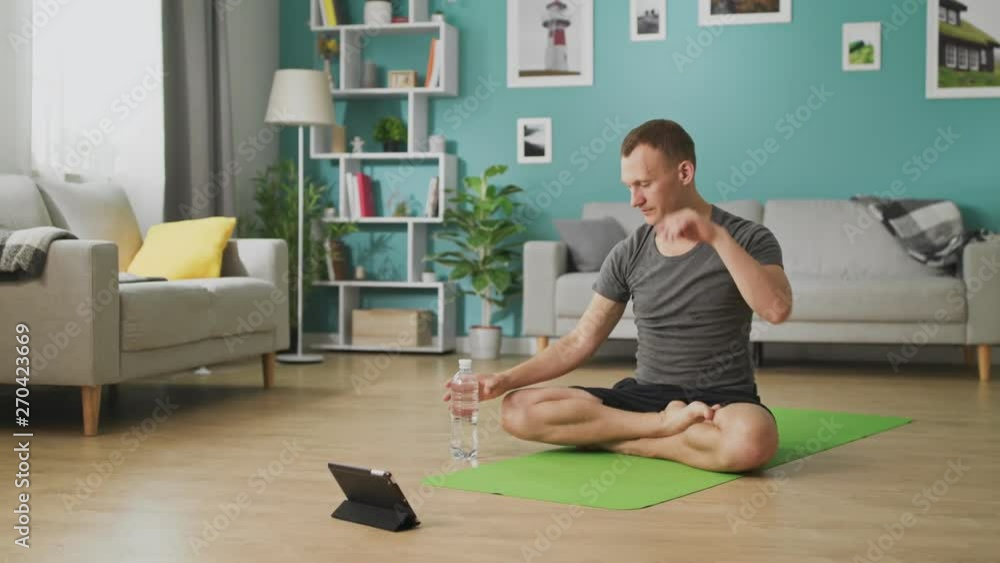 Man drinking water from a bottle during yoga classes online Man drinking water from a bottle during yoga classes online