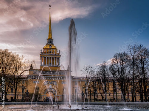 The facade and the ornate golden tower of the Admiralty Building in Saint Petersburg, Russia at dawn with a working fountain in the front of it