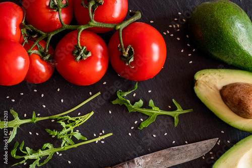 Tomatos and avocado on black table close up, colorful healthy food 