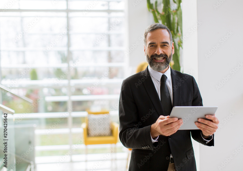 Handsome smiling mature businessman with tablet in the office working, reading or searching something Handsome smiling mature businessman with tablet in the office working, reading or searching something
