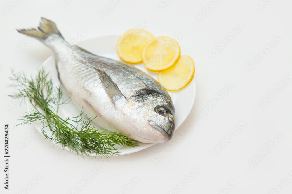 One raw fresh dorado fish in a plate with dill and lemon before cooking. One raw fresh dorado fish in a plate with dill and lemon before cooking.