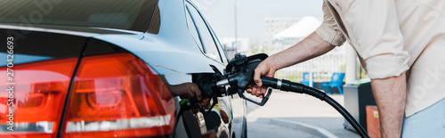 Foto Panoramic shot of man holding fuel pump and refueling black car