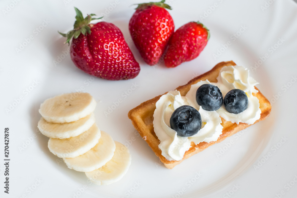 White plate with belgian waffles with strawberry, bananas and blueberries White plate with belgian waffles with strawberry, bananas and blueberries