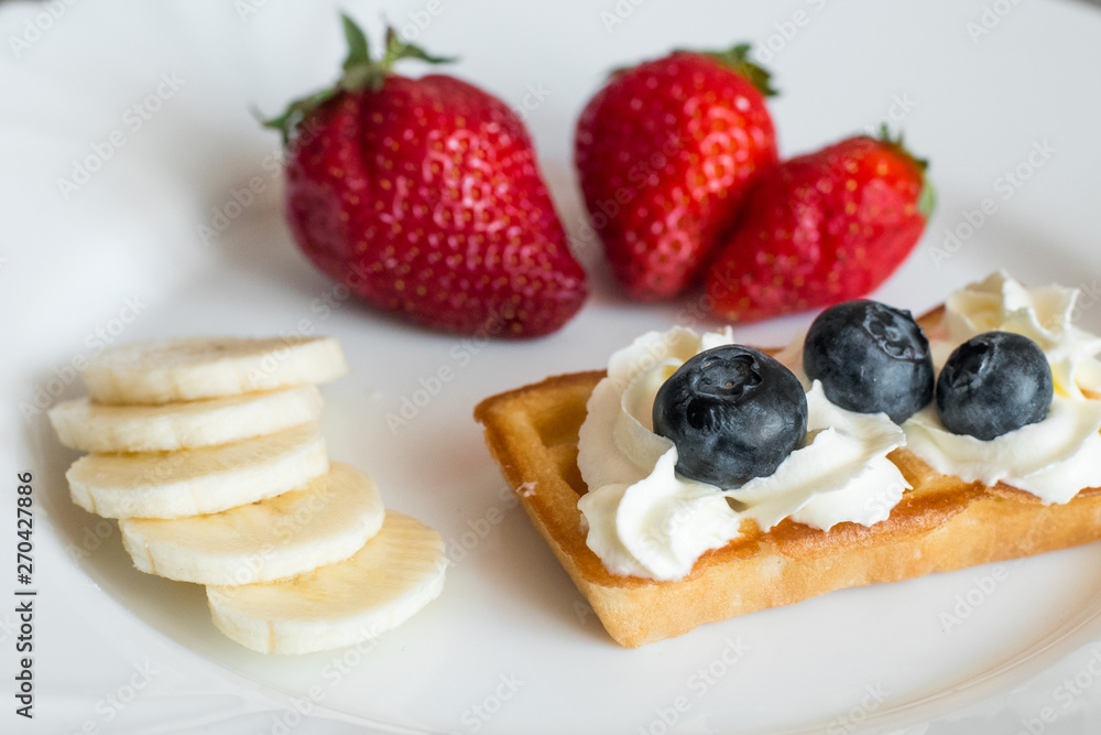 White plate with belgian waffles with strawberry, bananas and blueberries White plate with belgian waffles with strawberry, bananas and blueberries