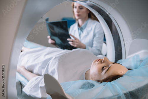 selective focus of radiologist holding x-ray diagnosis while patient lying on ct scanner bed during diagnostics photo