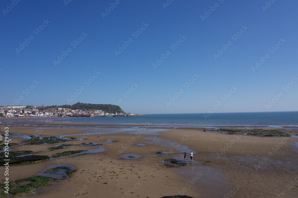 View along beachfront towards castle and harbour in Scarborough, Yorkshire, UK on a clear bright sunny blue sky day