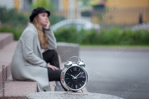 a girl sits on the steps and waits, a blurred silhouette, a clock in the foreground in focus, being late for a date, a long wait © Leka