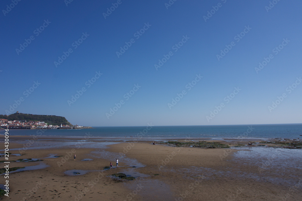 View along beachfront towards castle and harbour in Scarborough, Yorkshire, UK on a clear bright sunny blue sky day