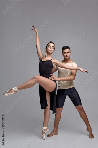 Fototapeta Naklejka Na Ścianę i Meble -  Two athletic modern ballet dancers are posing against a gray studio background.