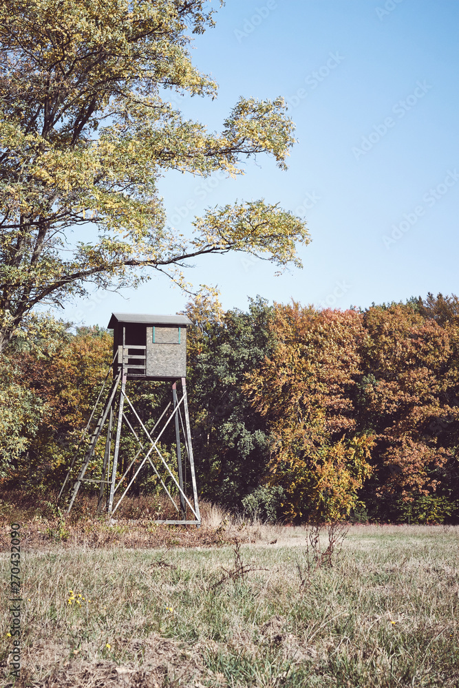 Retro toned picture of a wooden deer hunting pulpit at the edge of a forest and field.