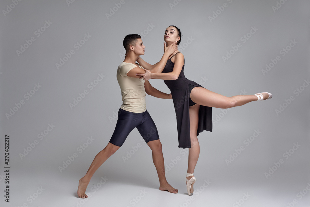 Two athletic modern ballet dancers are posing against a gray studio background. Two athletic modern ballet dancers are posing against a gray studio background.