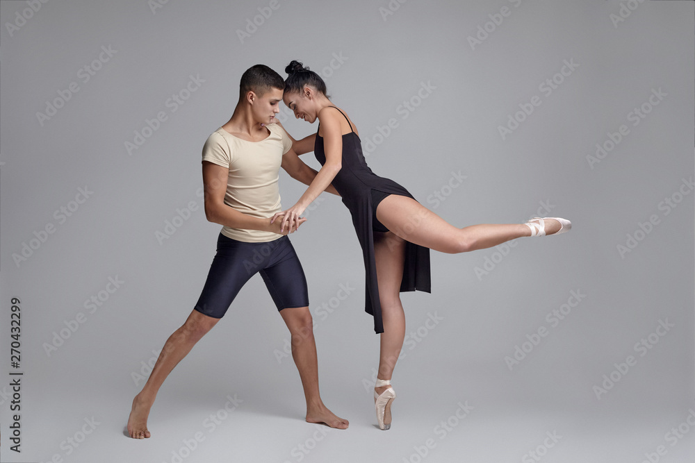 Fototapeta premium Two athletic modern ballet dancers are posing against a gray studio background.