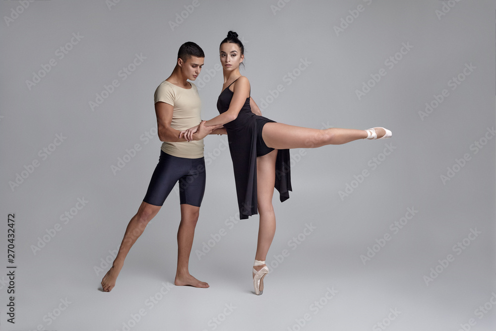 Two athletic modern ballet dancers are posing against a gray studio background. Two athletic modern ballet dancers are posing against a gray studio background.