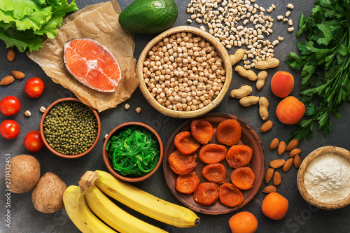 Healthy foods high in potassium. A variety of legumes, salmon, fruits, vegetables, dried apricots, seaweed chuka and nuts on a dark background. Top view, flat lay.