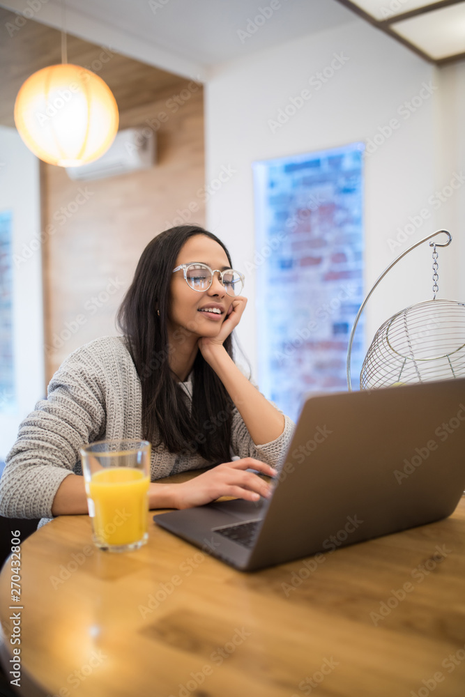 Portrait of adorable caucasian woman using laptop at table in kitchen interior while having breakfast at home Portrait of adorable caucasian woman using laptop at table in kitchen interior while having breakfast at home