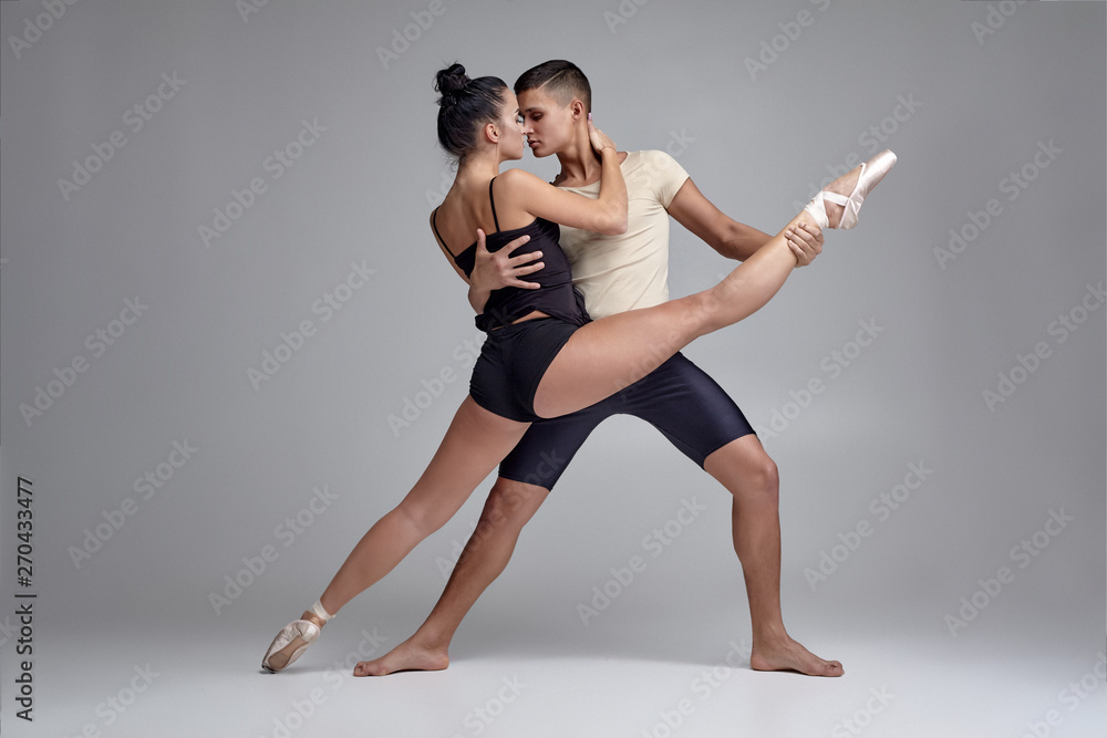 Two athletic modern ballet dancers are posing against a gray studio background.