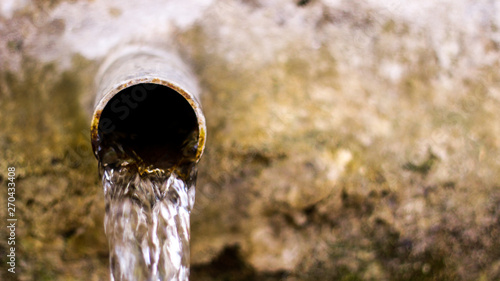 Water flow from old metal pipe. Blurred background. 