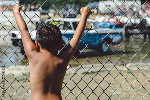 Poor kid with his hands on a fence watching an old police car.