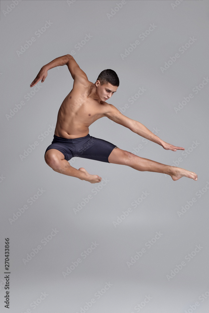 Photo of a handsome man ballet dancer, dressed in a black shorts, making a dance element against a gray background in studio. Photo of a handsome man ballet dancer, dressed in a black shorts, making a dance element against a gray background in studio.