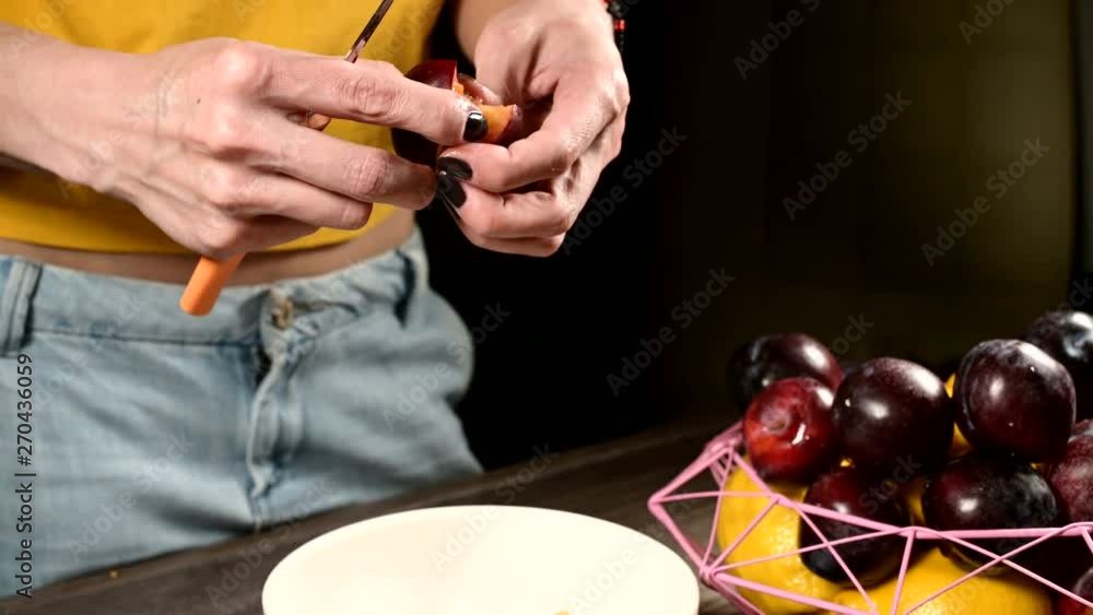 Close-up of female hands in a home kitchen are cutting fresh berries with a plum knife and taking a bone out of them next to a basket of lemons. The concept of healthy food and vitamins Close-up of female hands in a home kitchen are cutting fresh berries with a plum knife and taking a bone out of them next to a basket of lemons. The concept of healthy food and vitamins