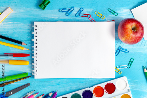 Notebook blank pages with colorful pencils, markers and pens composition Back to school concept with stationery office supplies on a blue wooden background with copy space close-up top view