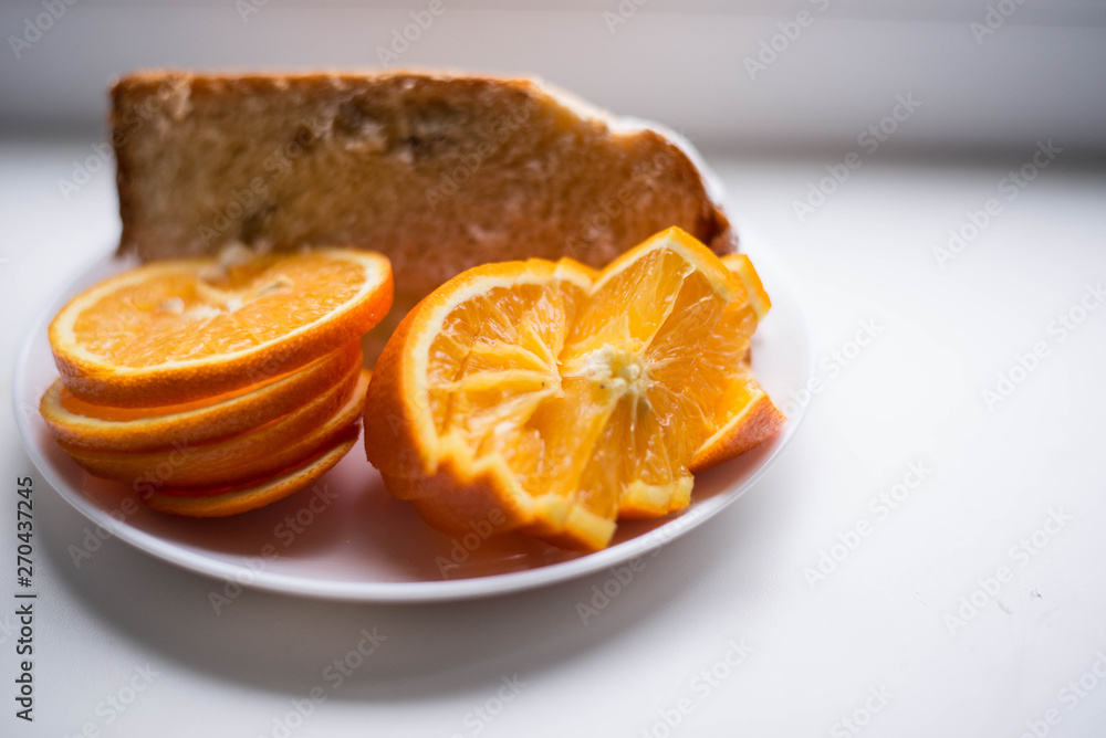 Oranges are sliced in a white plate. In the background there is also a piece of the pie Oranges are sliced in a white plate. In the background there is also a piece of the pie