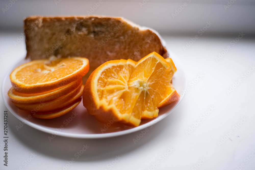 Oranges are sliced in a white plate. In the background there is also a piece of the pie Oranges are sliced in a white plate. In the background there is also a piece of the pie