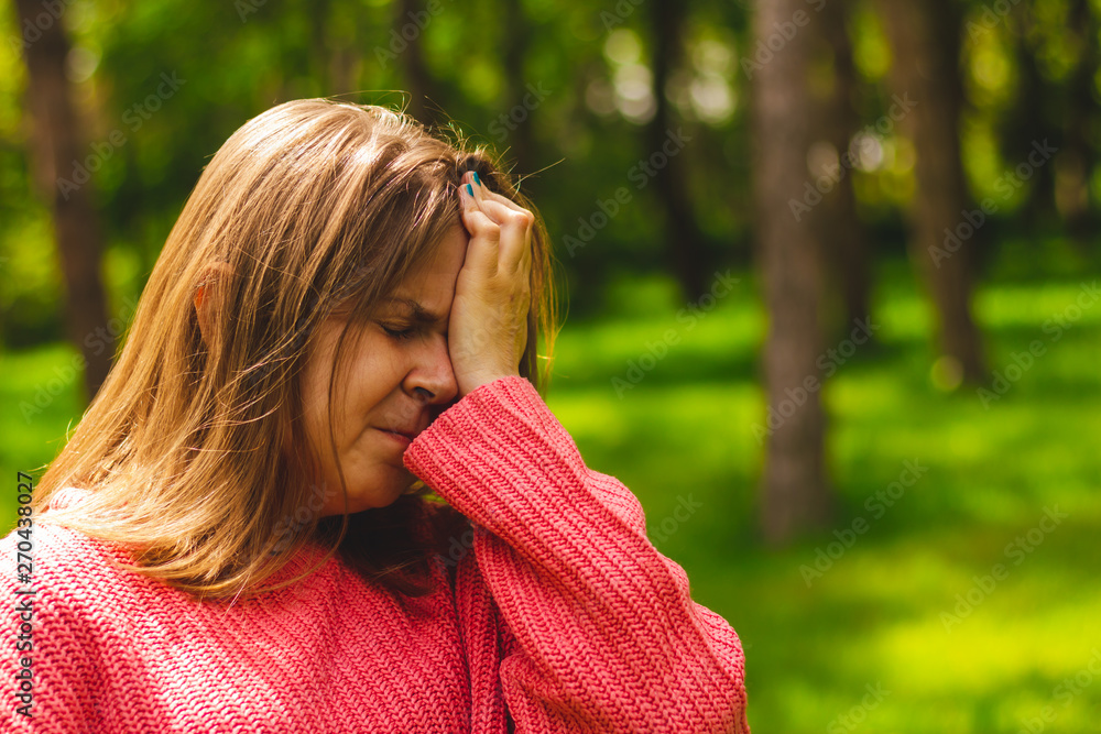 Young woman with short brown hair wearing a pink blouse holding one hand on her forehead while having a headache – Tired girl experiencing symptoms caused by stress Young woman with short brown hair wearing a pink blouse holding one hand on her forehead while having a headache – Tired girl experiencing symptoms caused by stress