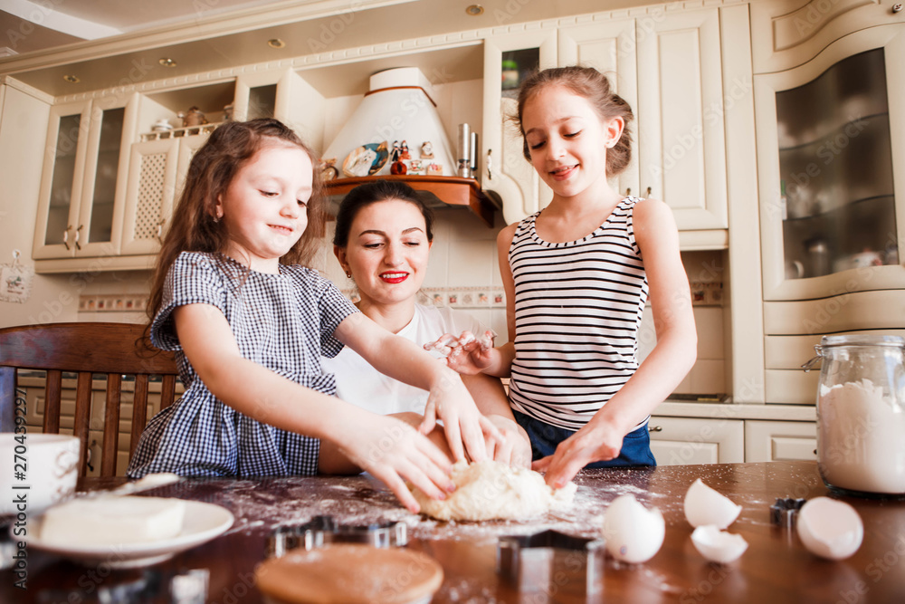 Fototapeta premium Mom and daughters prepare pastries in the bright classic kitchen. Creative mess on the table. Life style.
