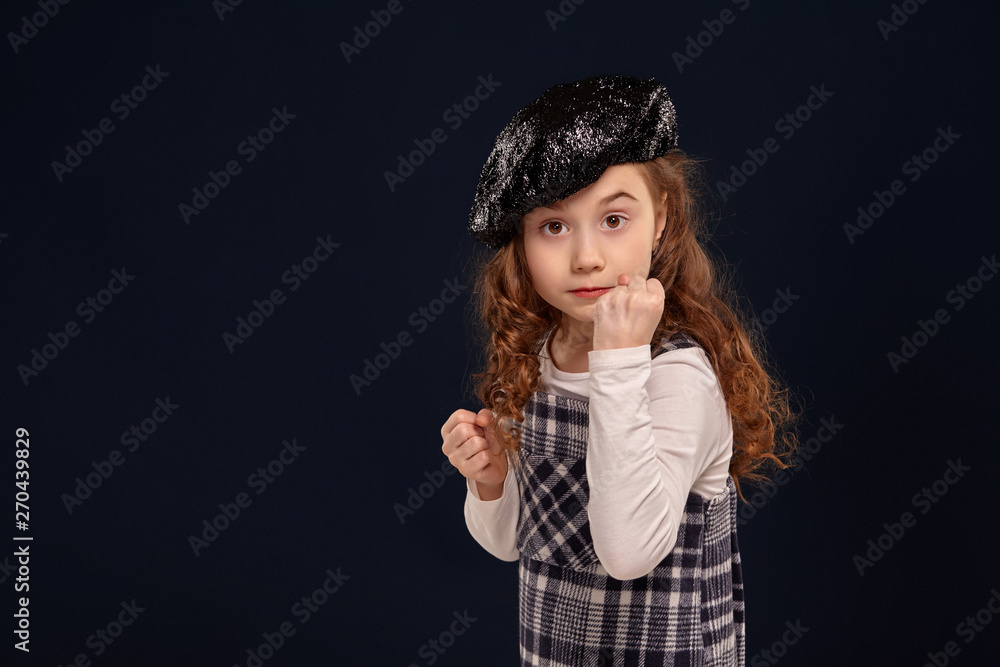 Stylish brunette kid is posing in studio on a black background. Children's fashion.