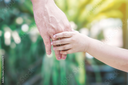hand of father and kid holding together with love over nature background © doucefleur