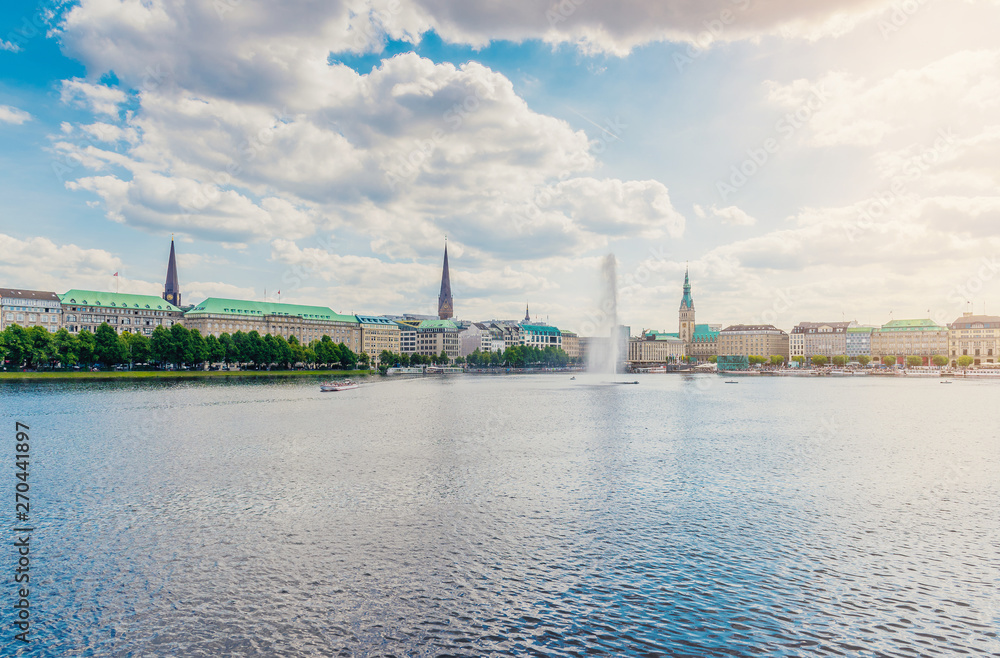 Hamburg cityscape on sunny day against blue sky with Alster lake and fountain in foreground