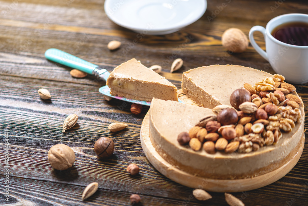 Fototapeta premium Nutty caramel cheesecake cake with topping of walnut, almond, hazelnut and macadamia on a dark wooden background.
