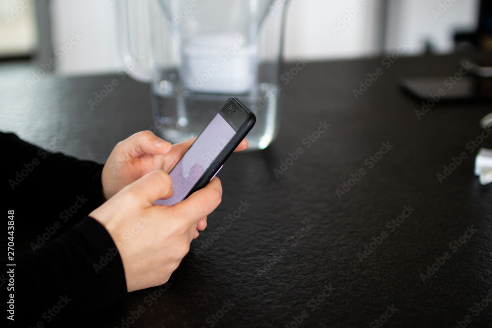 A woman while using her smartphone at home, black granite table and water in the background. Use your smartphone in your spare time