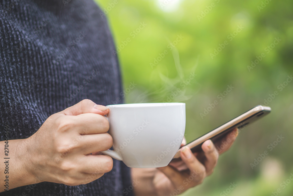 closeup woman hands holding smart phone and drinking hot coffee in the morning closeup woman hands holding smart phone and drinking hot coffee in the morning