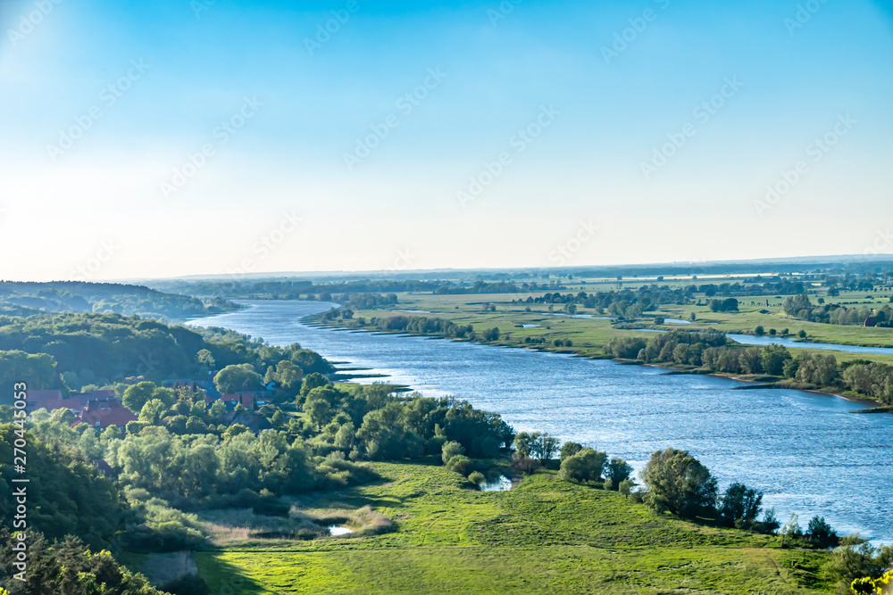 View over the Elbauen in Lower Saxony, Germany. You see a landscape with fields, meadows and the river Elbe under a blue sky. View over the Elbauen in Lower Saxony, Germany. You see a landscape with fields, meadows and the river Elbe under a blue sky.