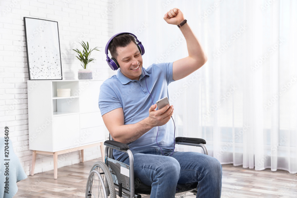 Happy man with headphones and mobile device in wheelchair at home Happy man with headphones and mobile device in wheelchair at home