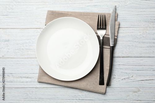 Stylish ceramic plate, napkin and cutlery on white wooden background, flat lay