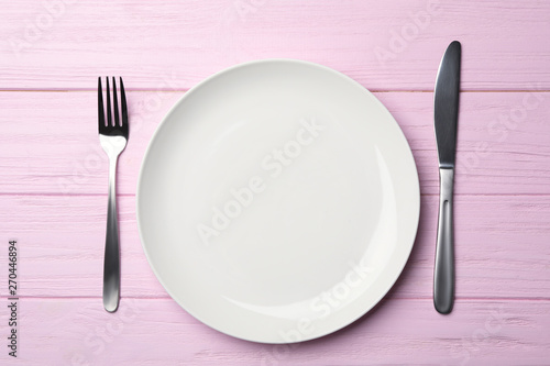 Stylish ceramic plate and cutlery on wooden background, flat lay