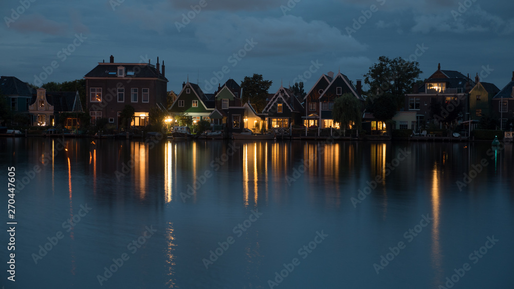 Obraz premium Night shot of houses in Dutch village on riverbank. Lights reflecting on water surface
