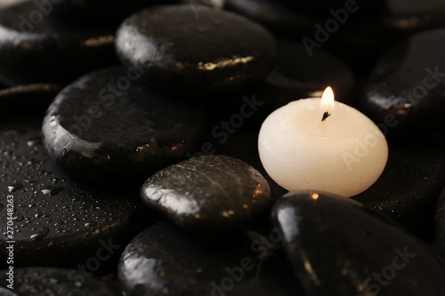 Small burning candle on beautiful wet spa stones, space for text