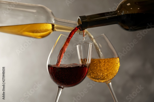 Pouring different wines from bottles into glasses on dark background