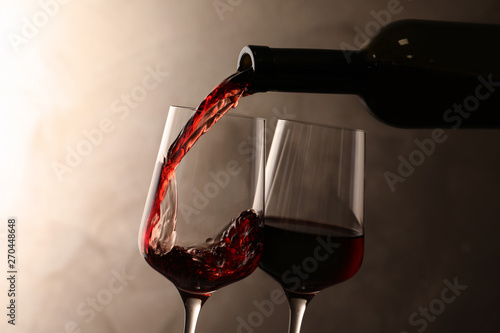 Pouring wine from bottle into glass on color background