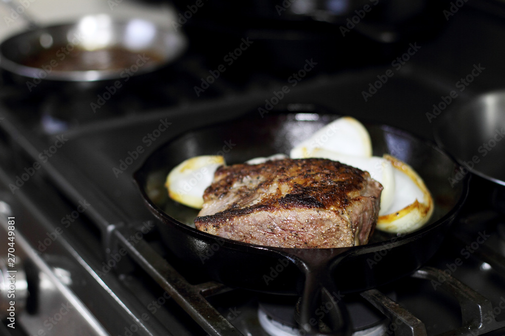 Sirloin steak frying in a cast iron pan with onions on the stove top.