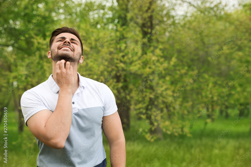 Young man scratching neck outdoors, space for text. Seasonal allergy Young man scratching neck outdoors, space for text. Seasonal allergy