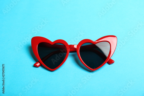 Red heart shaped sunglasses on color background, top view