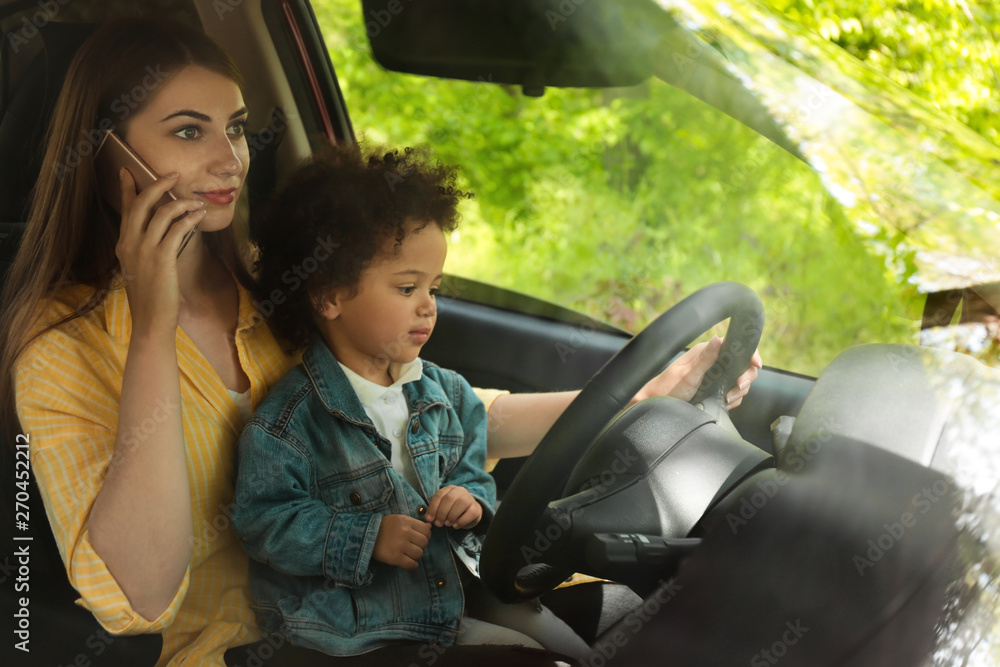 Mother with little daughter on knees driving car and talking by phone. Child in danger Mother with little daughter on knees driving car and talking by phone. Child in danger