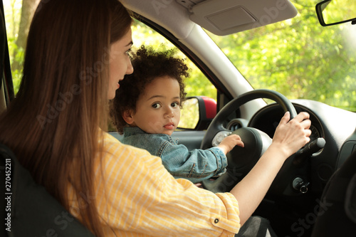 Mother with cute little daughter driving car together. Child in danger